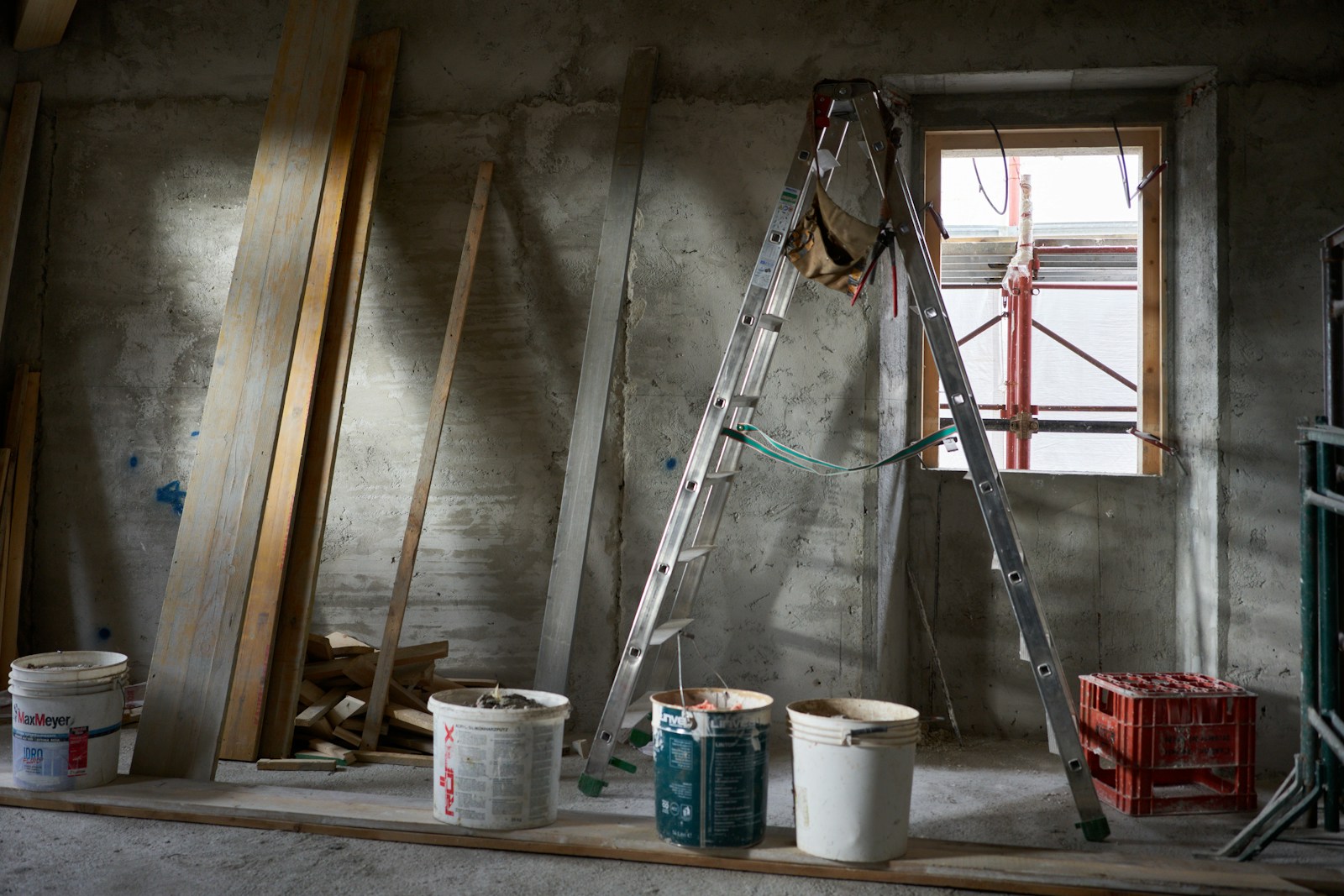 a ladder and buckets of paint in a room under construction