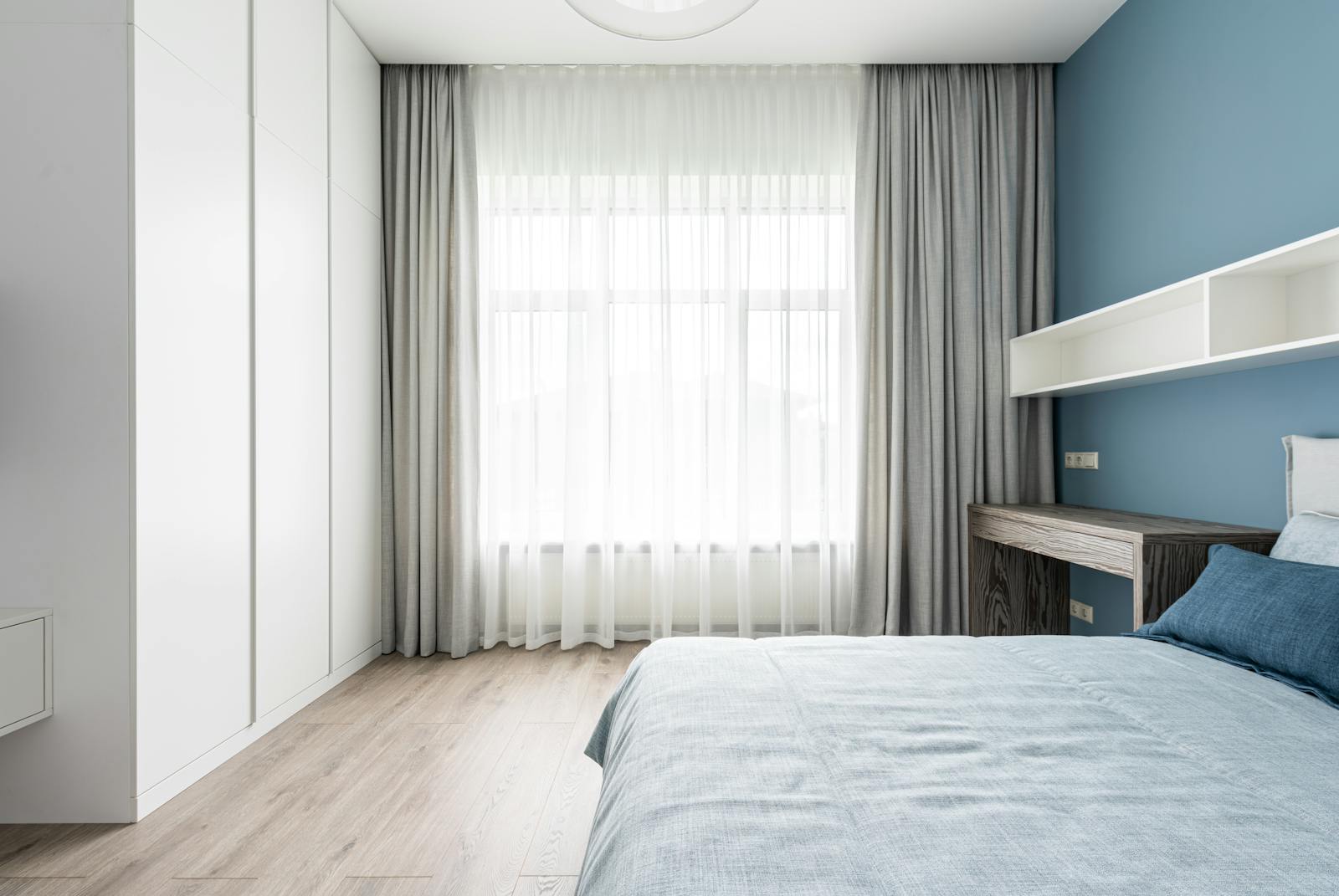 Modern interior of contemporary bedroom with comfortable bed and empty white shelves near window