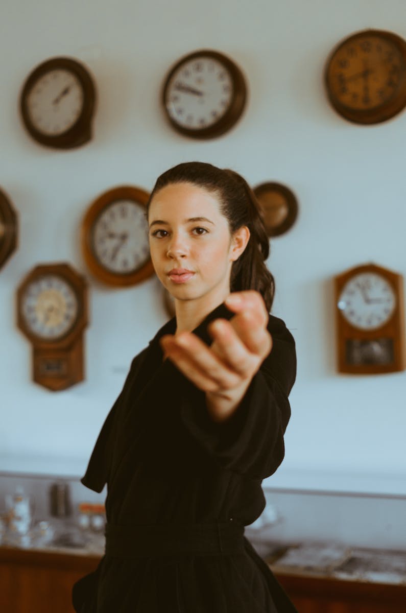 Artistic portrait of a woman indoors surrounded by vintage clocks, creating a timeless feel.